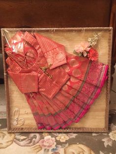 pink and red saree with flowers on it in a wooden frame next to a table