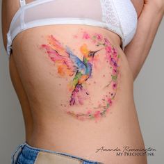 a woman's stomach with a colorful hummingbird tattoo on her side and the bottom part of her belly