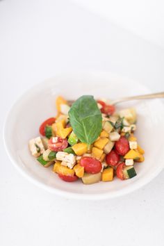 a white plate topped with salad and a green leaf on top of the bowl next to it