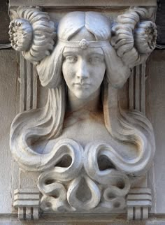 a close up of a statue on the side of a building with flowers in her hair