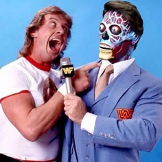 two men in suits and one is holding a microphone with his face painted like a wrestler