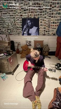 a woman sitting on the floor with a guitar in front of her and pictures behind her