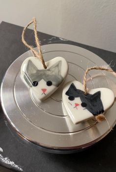 two heart shaped cookies decorated with cats on top of a silver plate and twine