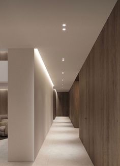 a long hallway with white walls and wooden paneling on the sides is lit by recessed lighting