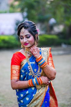 a woman in a blue and red sari with her hands on her chest, looking at the camera