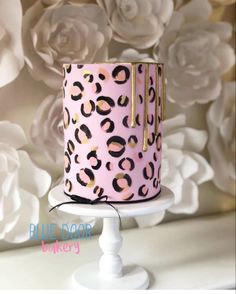 a pink leopard print cake with gold accents on a white pedestal in front of flowers