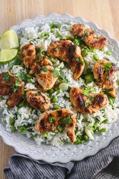 a white plate topped with rice and chicken on top of a wooden table next to a lime wedge