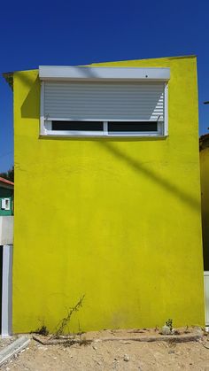 a yellow building with a white window next to a green wall and a red fire hydrant