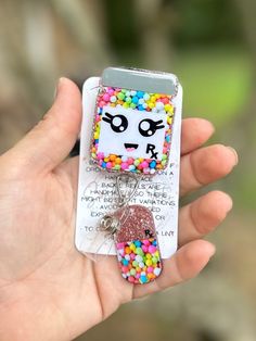 a hand holding a cell phone charm with sprinkles on it's face