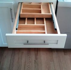 an open drawer in the middle of a white kitchen cabinet with drawers on both sides