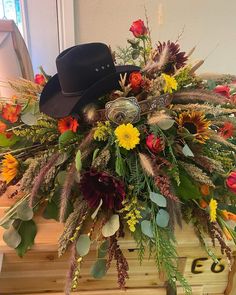 an arrangement of flowers, feathers and a cowboy hat on top of a wooden box