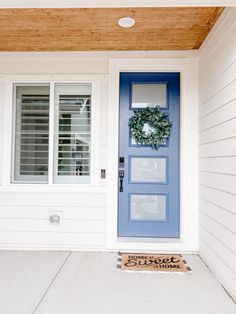 a blue front door with a wreath on it and a welcome mat in front of it