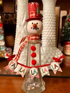 a snowman is sitting on top of a glass bottle with name tags attached to it