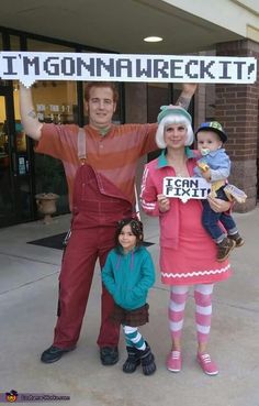 a man and woman holding up a sign while standing next to two children in front of a building