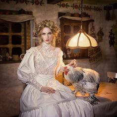 a woman in a white dress sitting on a table with a chicken next to her