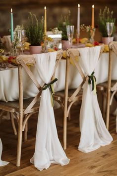 the table is set with white linens and decorated with flowers, candles and greenery