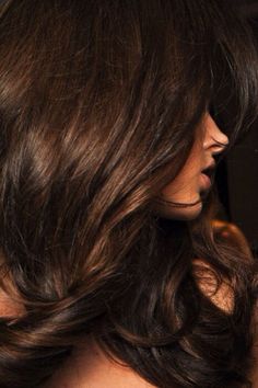 a woman with long dark brown hair is looking at her cell phone while she's in the mirror