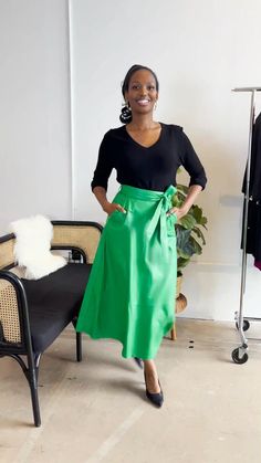 a woman standing in front of a chair wearing a green skirt and black top with her hands on her hips