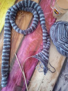 yarn and scissors on a wooden table next to a ball of yarn, with a cup of coffee in the background