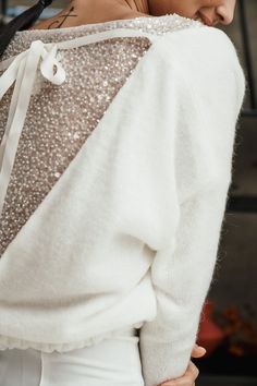 a woman with her back turned to the camera, wearing white pants and a sweater