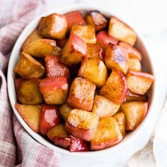 a white bowl filled with cooked potatoes on top of a table next to a fork