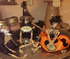 three skeleton figurines sitting on top of a metal table with halloween decorations in the background