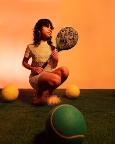 a woman kneeling down with a tennis racket in her hand next to two balls