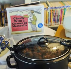 a slow cooker on a table with a book about cloudy with chance of meatballs