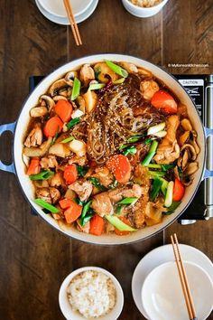 a pan filled with meat and veggies on top of a table next to bowls of rice