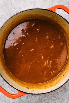 a pot filled with brown liquid sitting on top of a cement floor next to an orange spatula