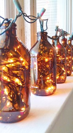 several glass bottles with lights in them sitting on a table next to a window sill