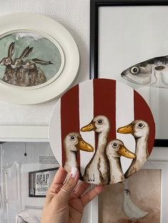 a person holding up two ducks in front of some pictures