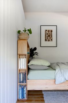 a bedroom with a bed, bookshelf and plant on the wall next to it