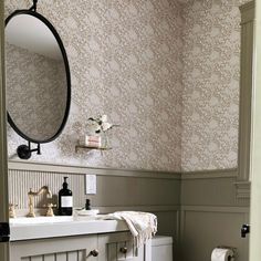 a white toilet sitting next to a bathroom sink under a mirror in a room with wall paper on the walls