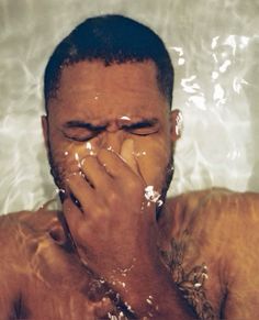 a shirtless man covers his face in the water