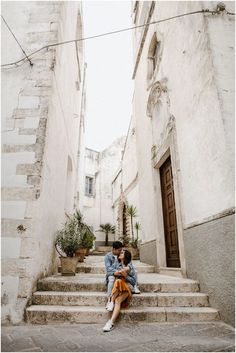 two people sitting on steps in front of an old building with potted plants next to them