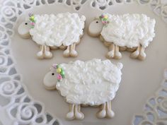 four decorated sheep cookies sitting on top of a white doily covered platter,