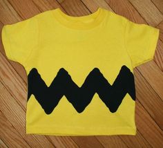 a child's yellow shirt with black mountains on the front and bottom, sitting on a wooden floor