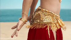 a woman in gold and red is standing on the beach with her hands behind her back