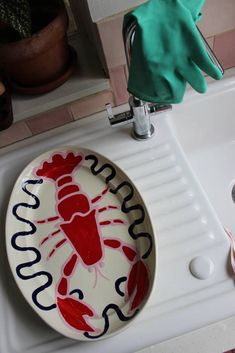 a bathroom sink with a lobster painted on the bowl next to a green rubber glove