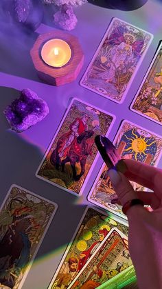 a person holding a pen in front of some cards on a table with a candle