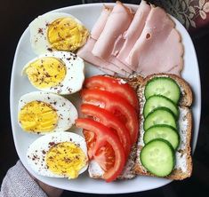 a white plate topped with eggs, tomatoes and cucumbers next to slices of tomato