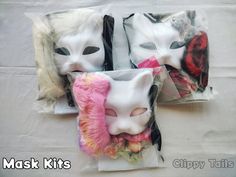 three white masks with pink flowers in them on top of a cloth covered tablecloth