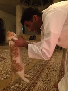 a man in white shirt petting a cat on top of a carpeted floor