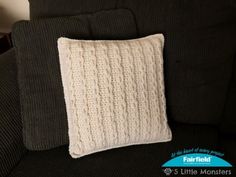 a white knitted pillow sitting on top of a black couch