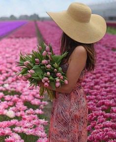 a woman in a large field with pink tulips and a straw hat on her head