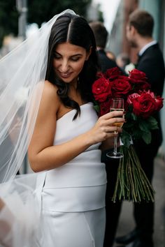 a woman in a white dress holding a bouquet of red roses and looking at her phone