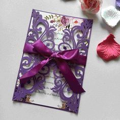 a purple wedding card with a bow on it next to some pink flowers and petals