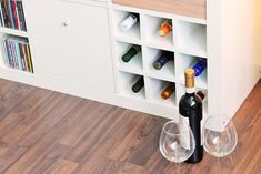 two wine glasses are sitting on the floor next to a cabinet with bottles and corks