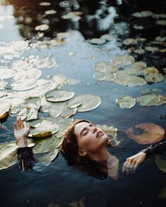 a woman floating on top of a body of water surrounded by lily pads